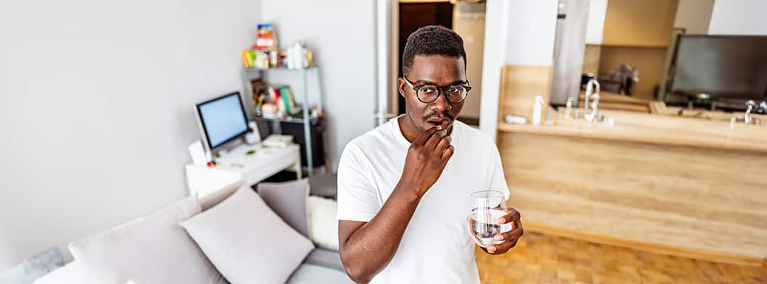 Man holding glass of water and taking a collagen supplement