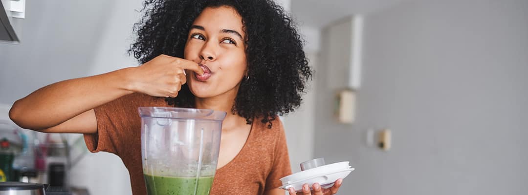 Woman tasting vegan smoothie from blender