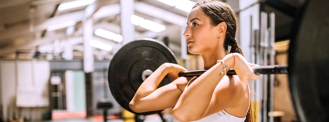 Woman using BCAAs to recover from lifting weights performing barbell overhead press